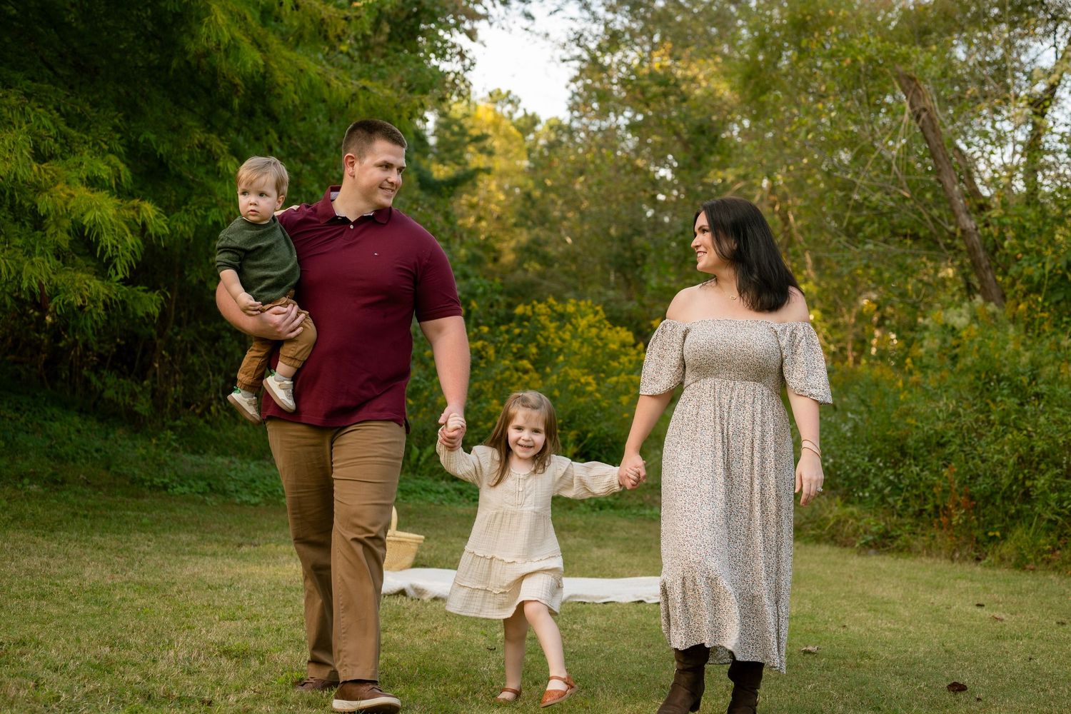 A group in coordinating burgundy and beige outfits poses together in a sunlit grassy field during golden hour.