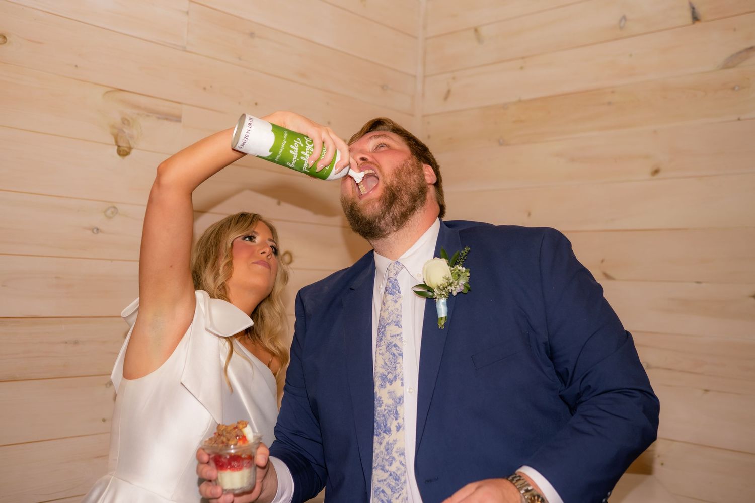 Bride and groom playfully drinking canned beverages at wedding reception.