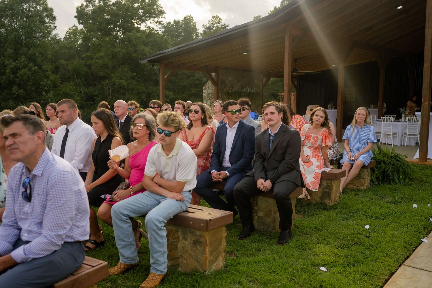 Guests seated outdoors on wooden benches at an elegant garden wedding ceremony venue.