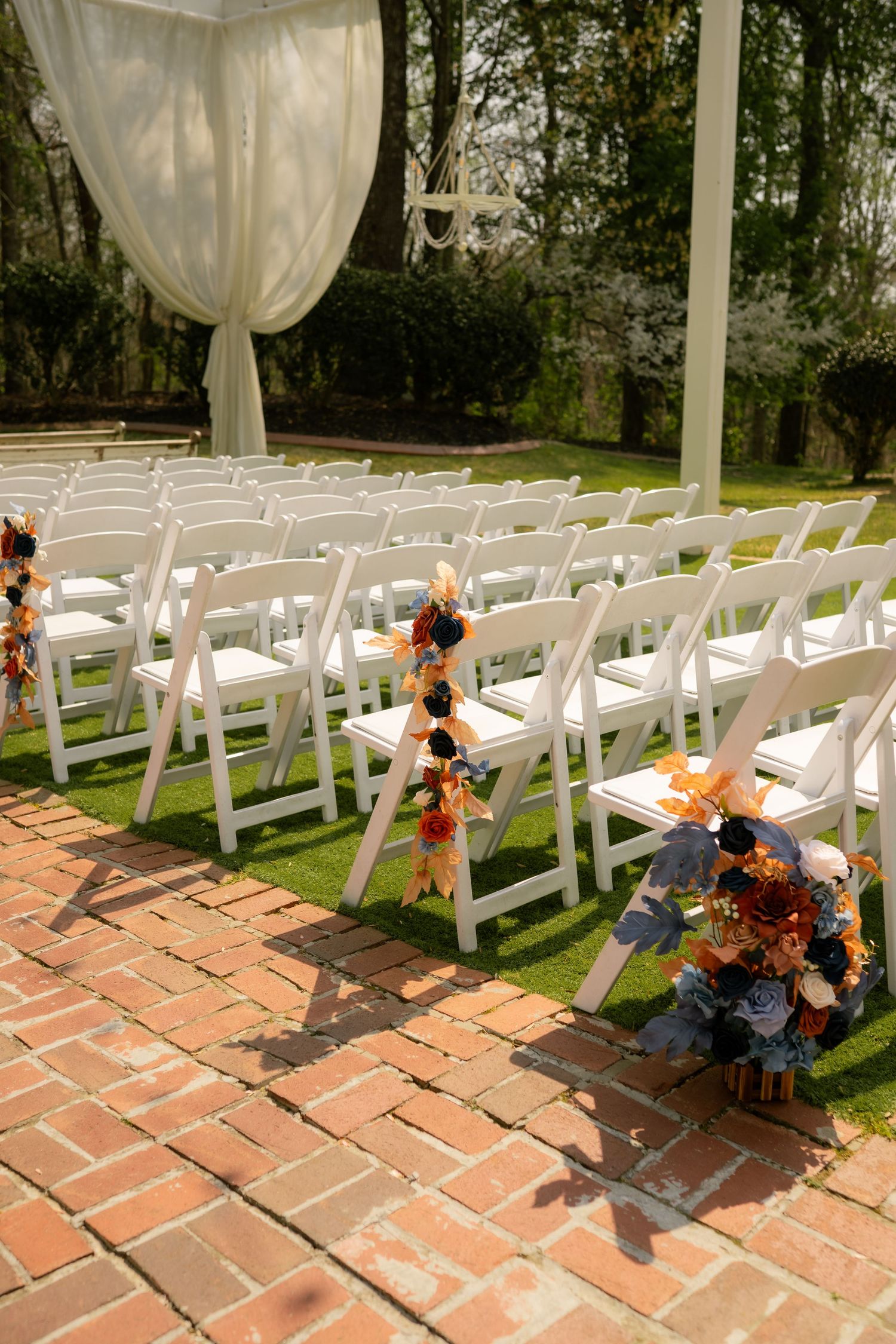 Outdoor wedding ceremony setup with white folding chairs, brick aisle, and colorful floral arrangements in orange and blue.