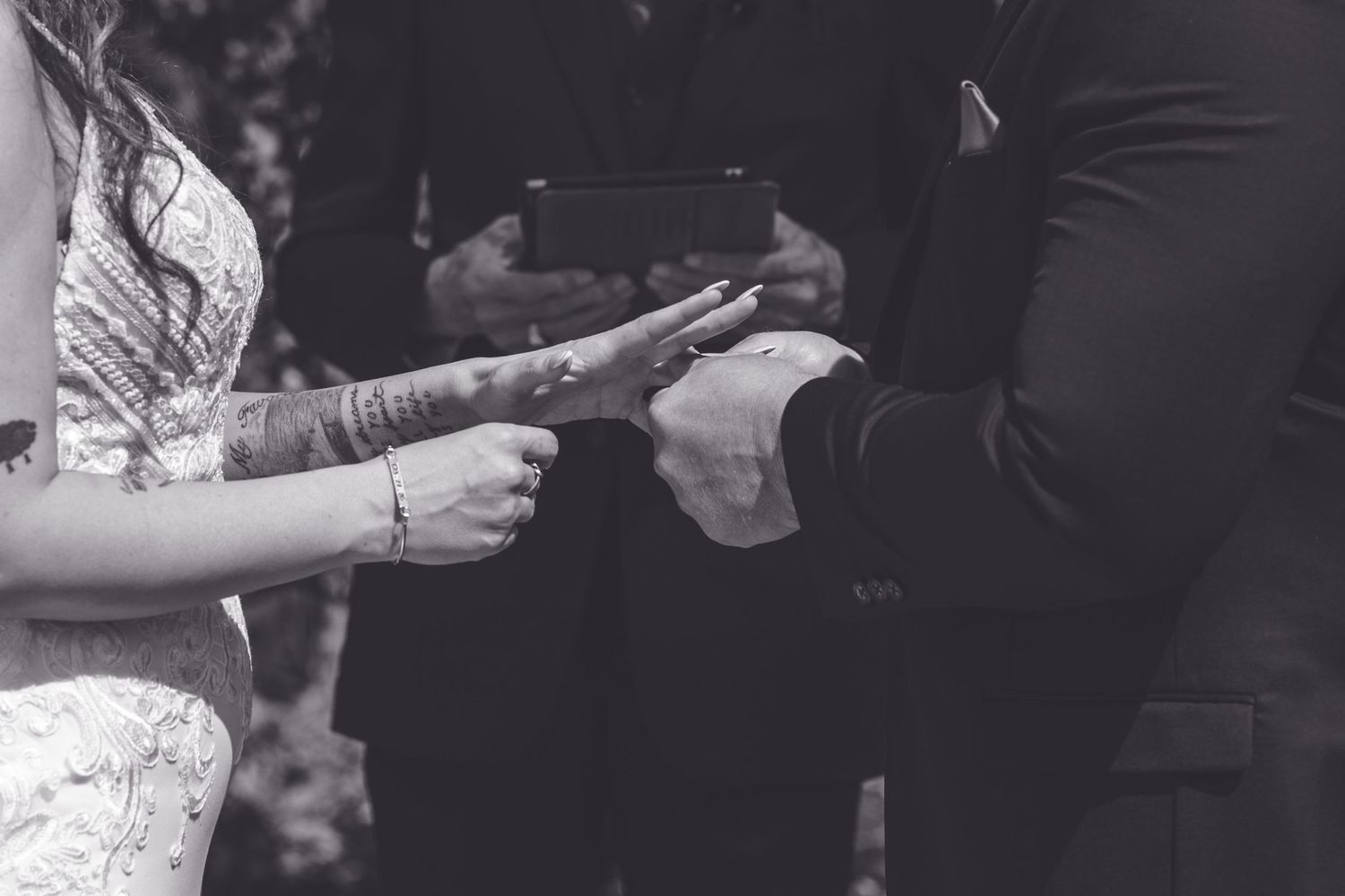 Black and white wedding photo of bride and groom exchanging rings during ceremony, bride has henna tattoos on hands.