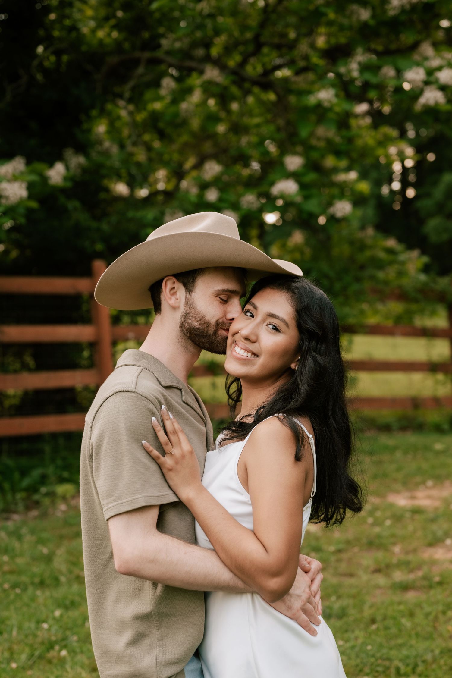 A romantic couple embraces outdoors on a sunny day with wooden fencing and greenery in the background. in North Georgia