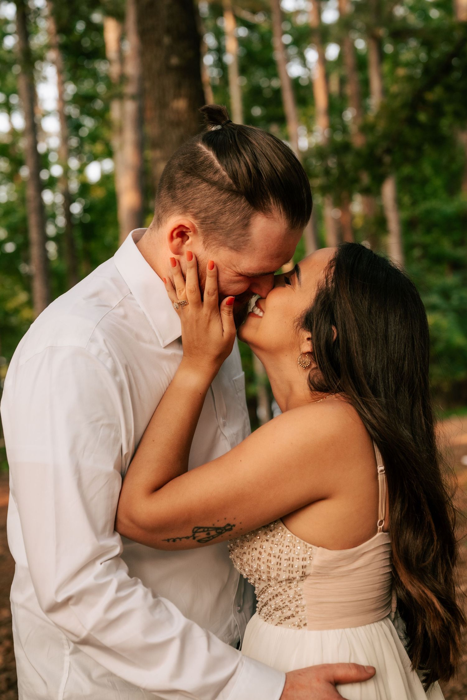 A romantic kiss between a couple in formal attire surrounded by a lush green forest setting.in North Georgia. True to color