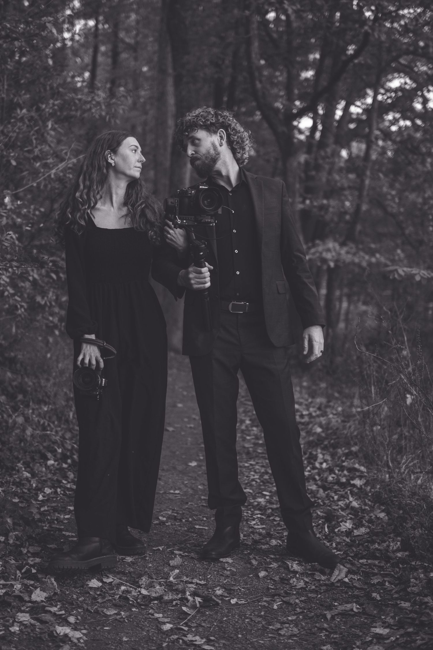 A couple in dark clothing shares an intimate moment together in a moody forest setting. Southern Pines, NC