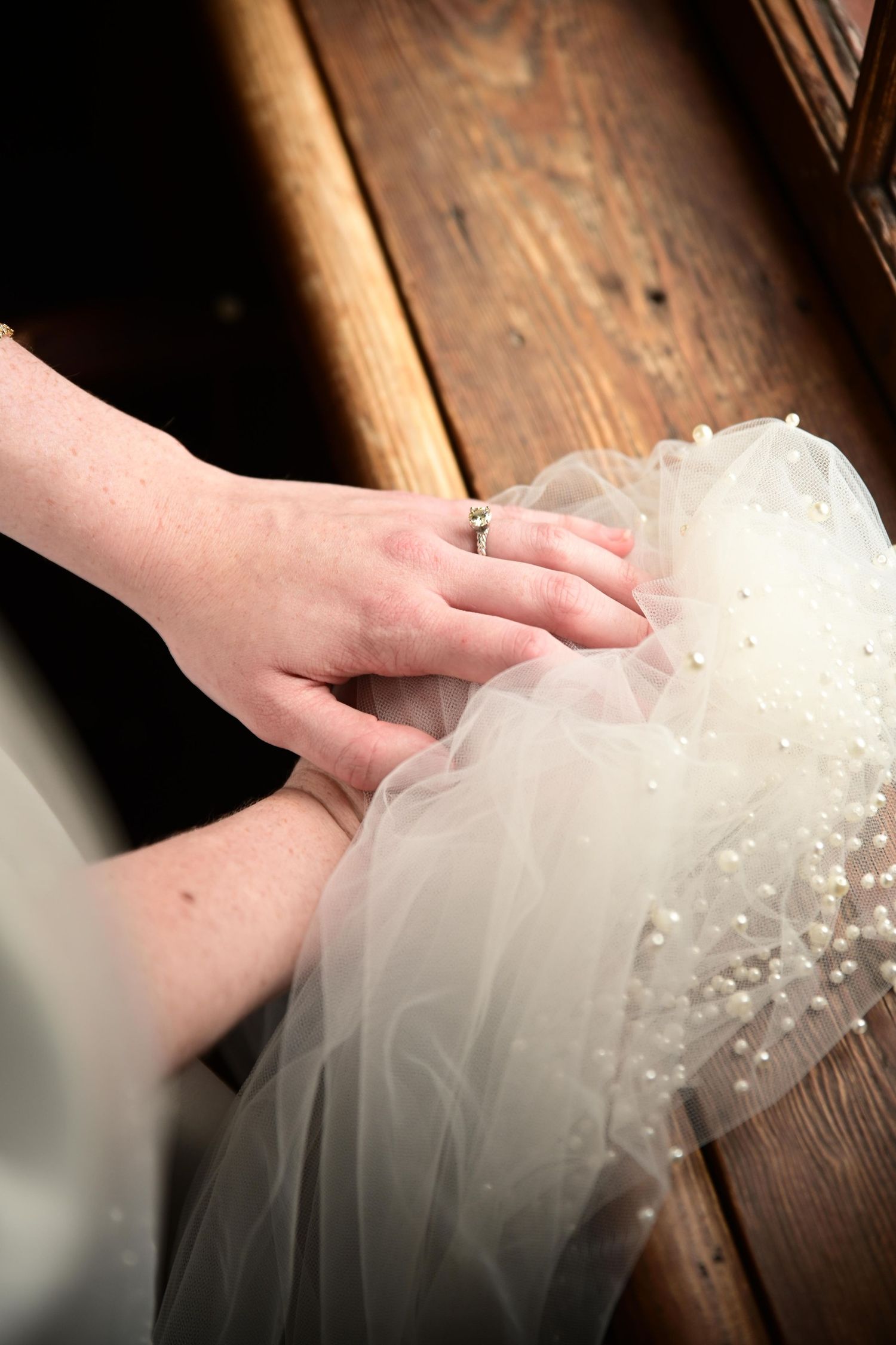 Close-up of bride's hand with engagement ring resting on pearl-trimmed white wedding veil.
