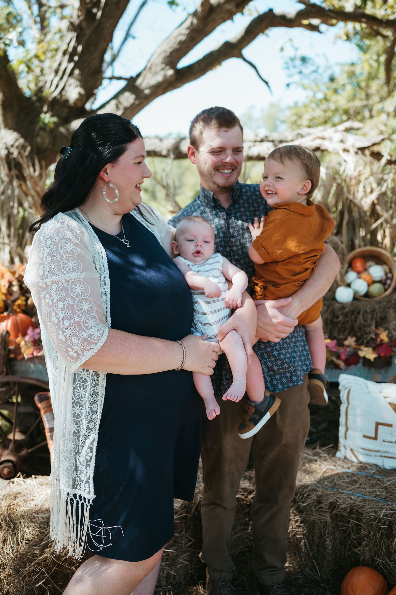 A mother and father smile and embrace their two boys during a fall photography session