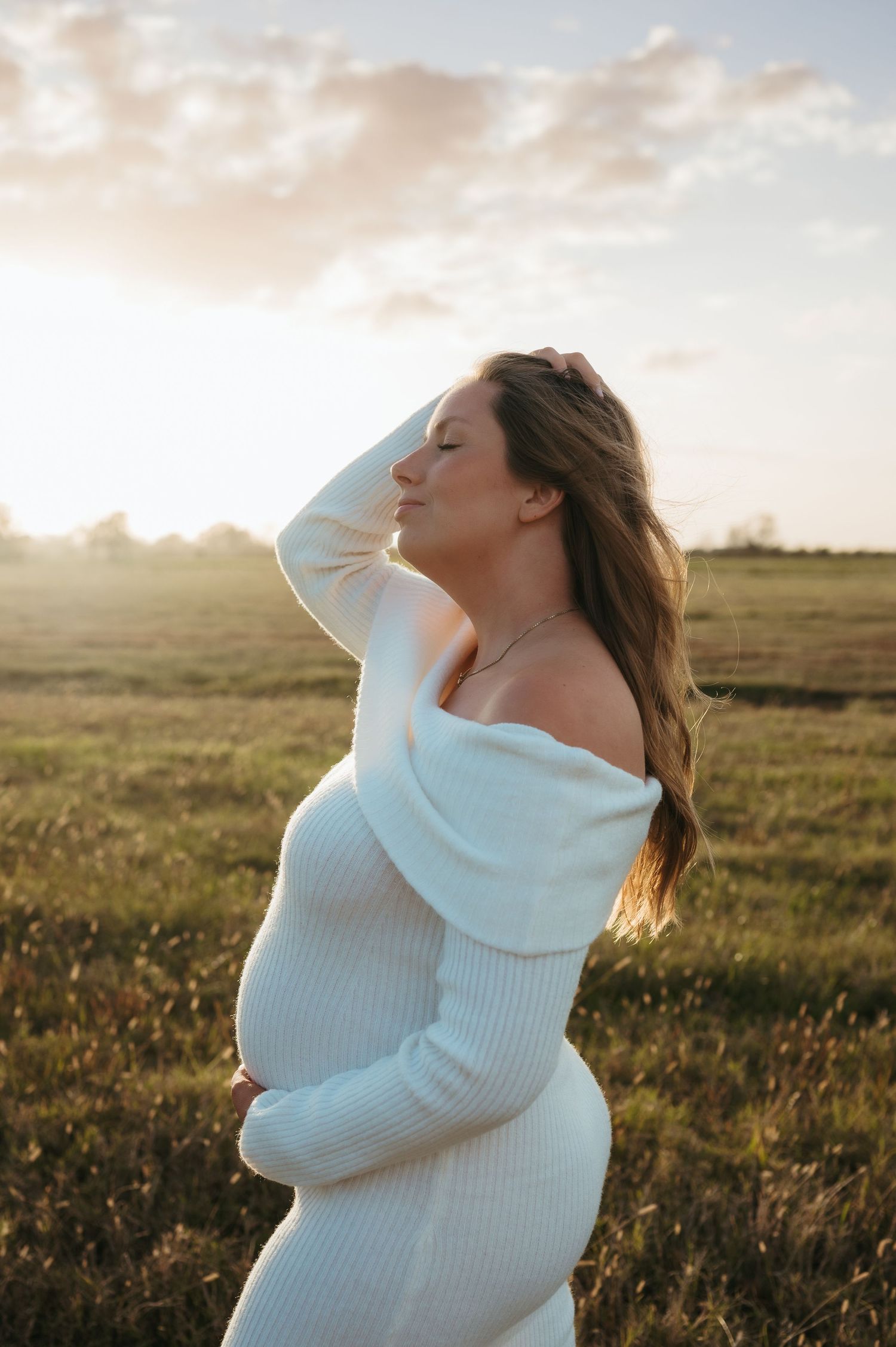 A mother to be basks in the sunlight during her maternity session while holding her growing belly
