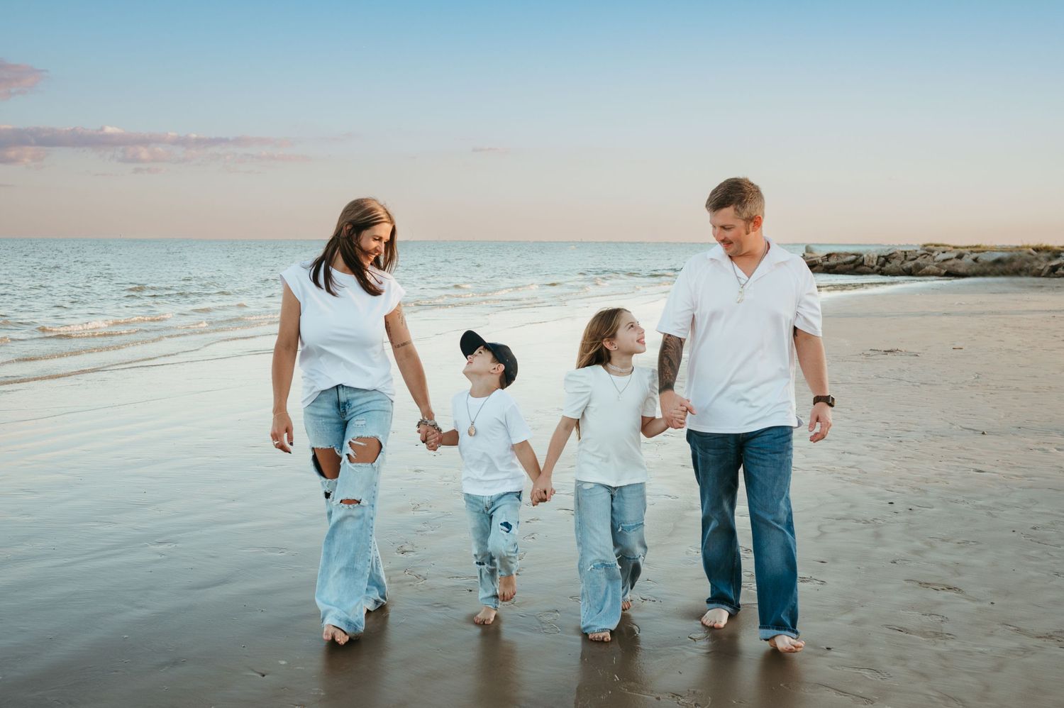 A family walks along a Texas beach smiling and holding hands during a family session