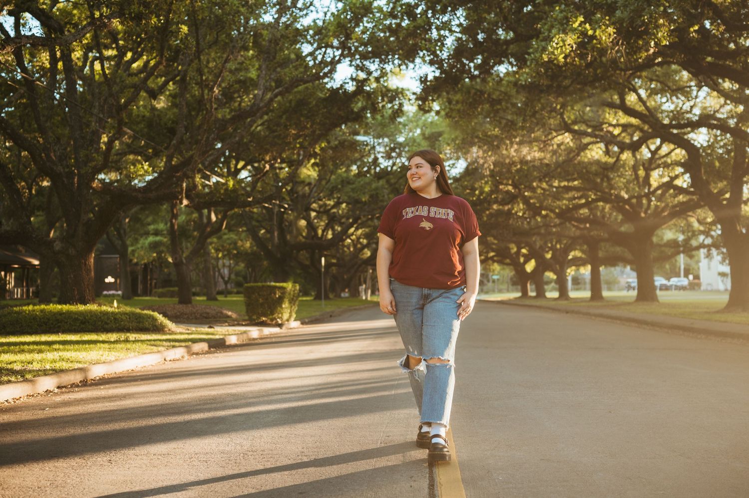 A senior walks among the oak trees in her college tee during her senior photography session