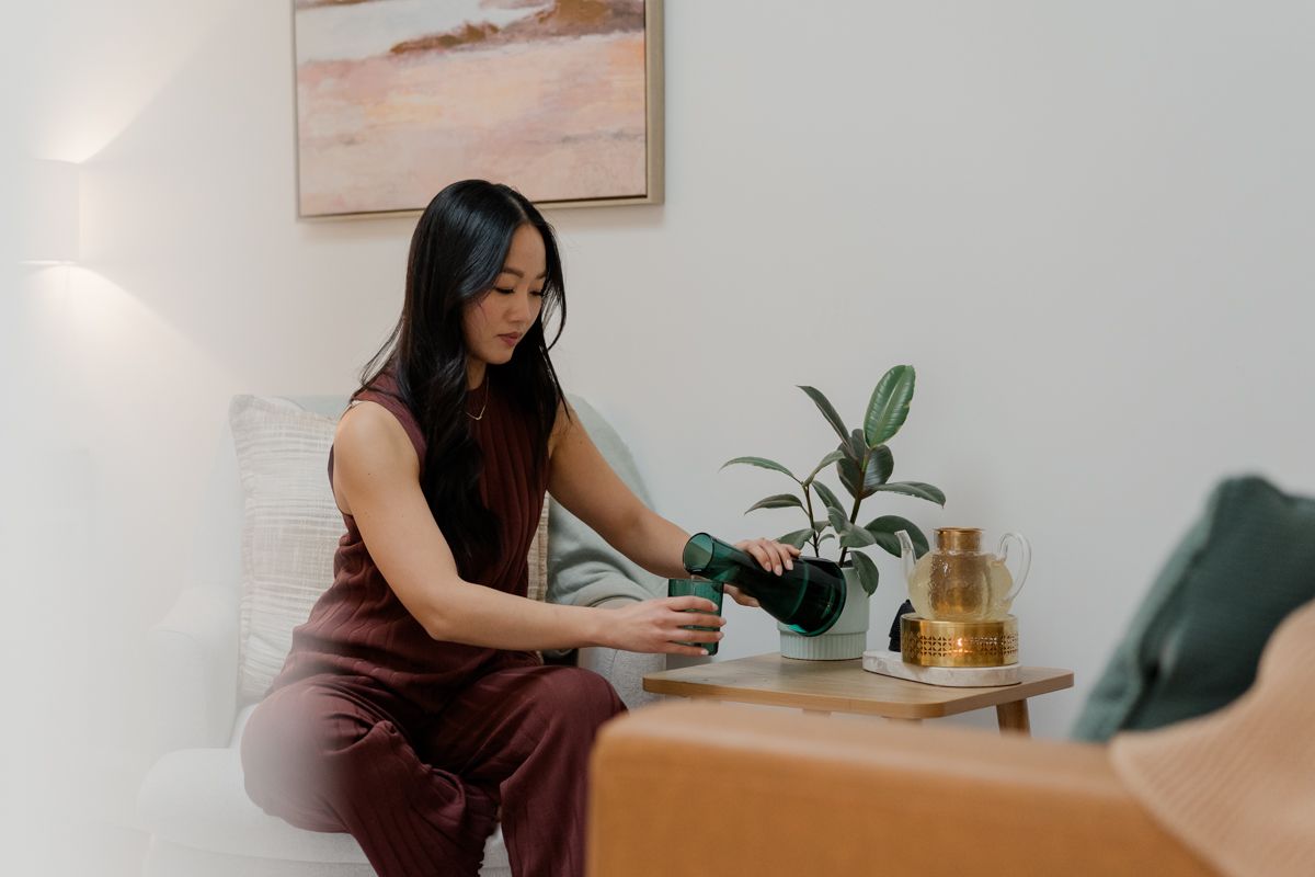 Woman in burgundy outfit tending to plant on wooden side table in modern interior.