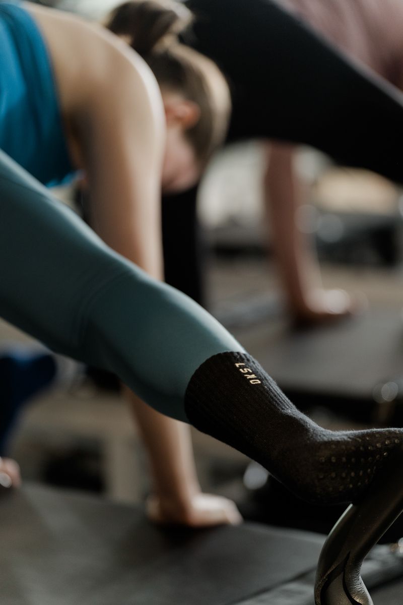 People performing Pilates exercises on reformers wearing LSND grip socks in studio class.