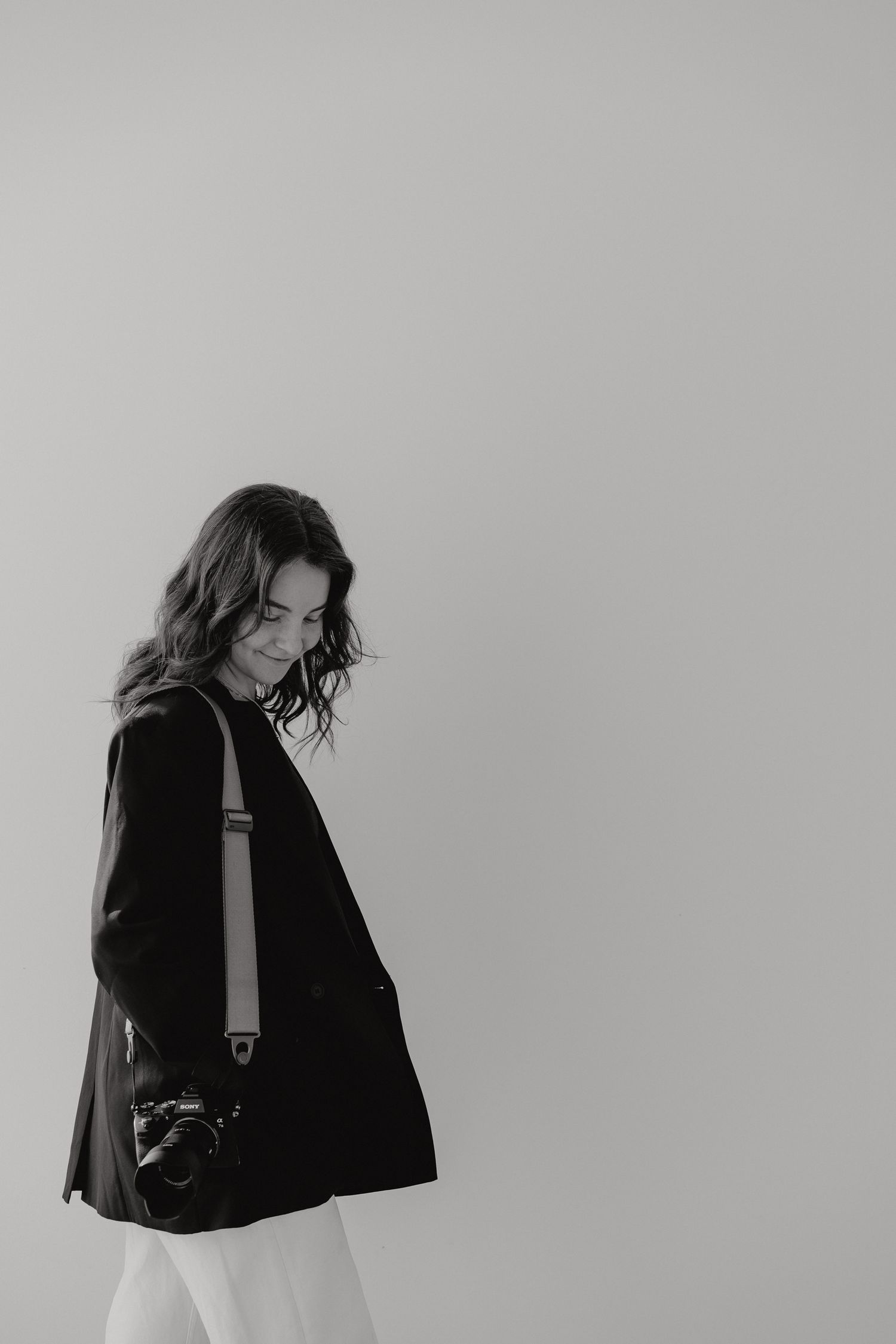 Young woman in black jacket carrying camera looking down in black and white portrait photo.