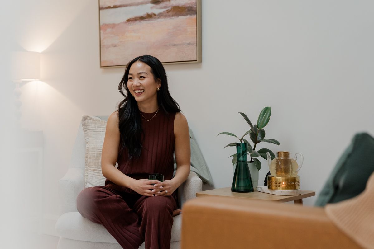 Woman in burgundy outfit sitting on white sofa smiling in bright modern therapy room.