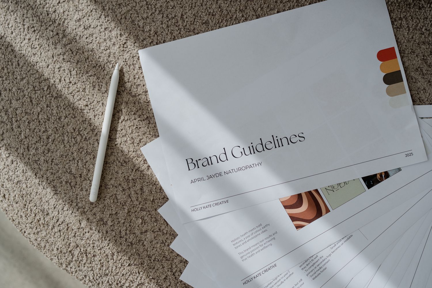 Brand guidelines documents with color swatches and pencil arranged on textured carpet surface.