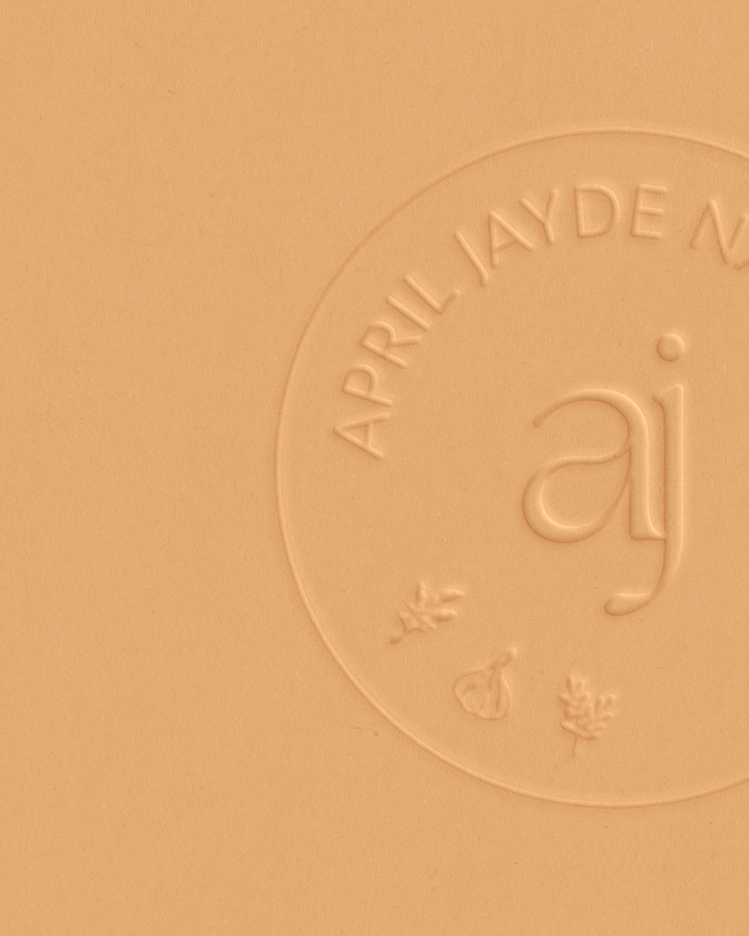 Close-up of embossed April Jayde Naturopathy circular logo stamp on warm golden orange surface.