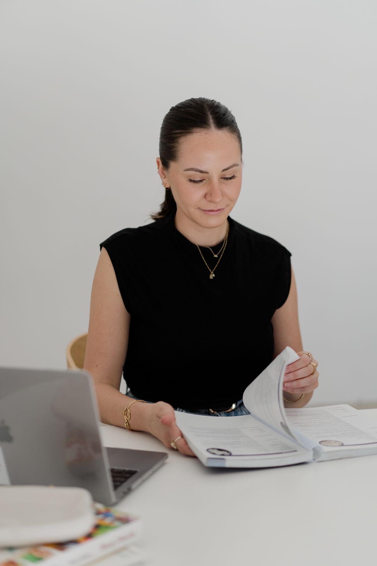 Woman in black top reading documents at white desk with laptop in bright office.