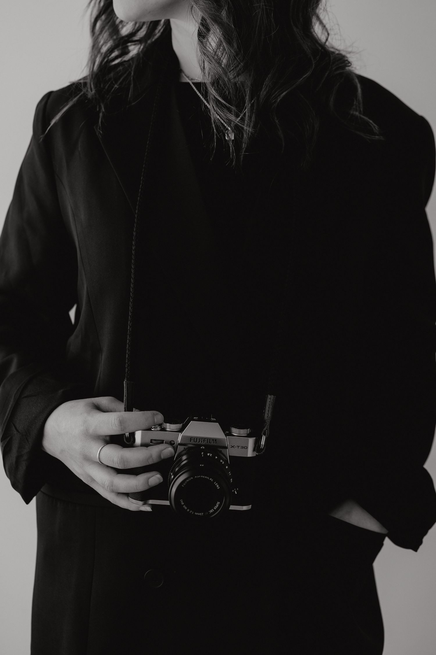 Woman in black blazer holding a vintage film camera, elegant black and white portrait.