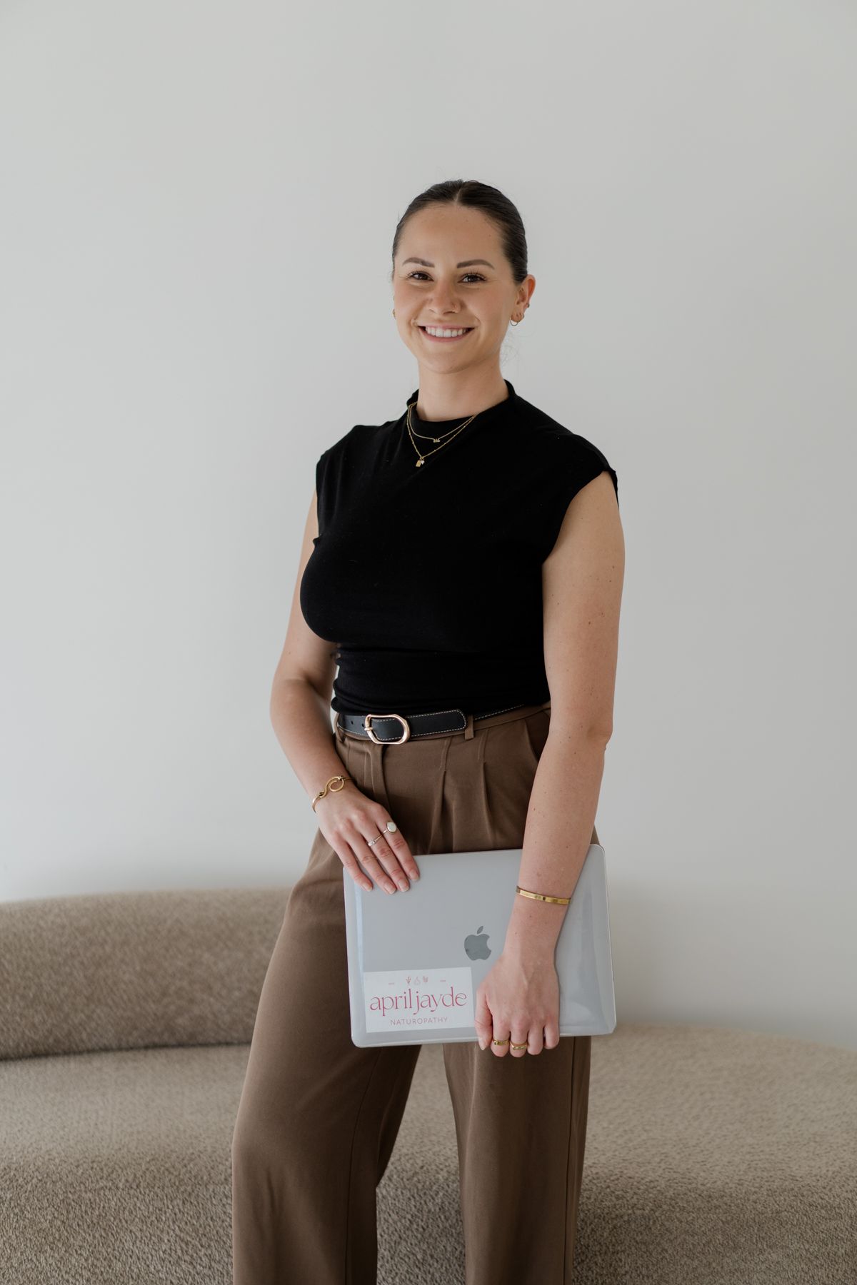 Smiling woman in black sleeveless top holds an Apple MacBook laptop with an aprildyde sticker.