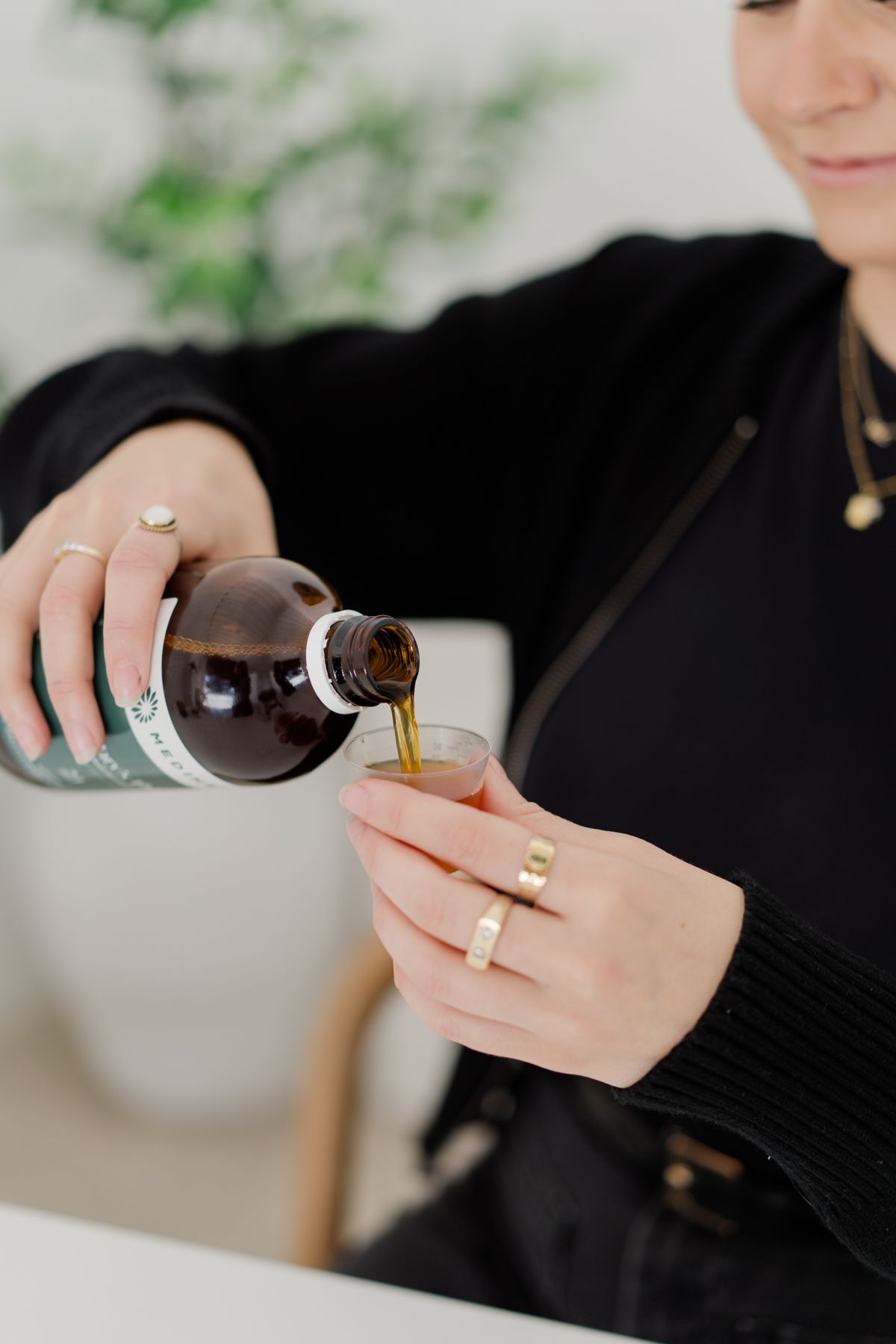 Close-up of hands pouring dark liquid herbal tincture from a brown bottle into a small glass cup.