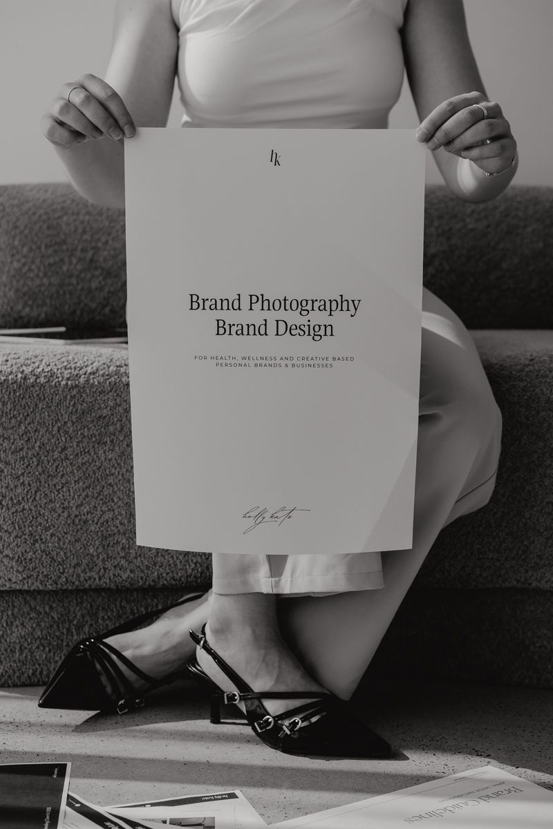 Black and white image of woman holding white poster reading Brand Photography Brand Design.