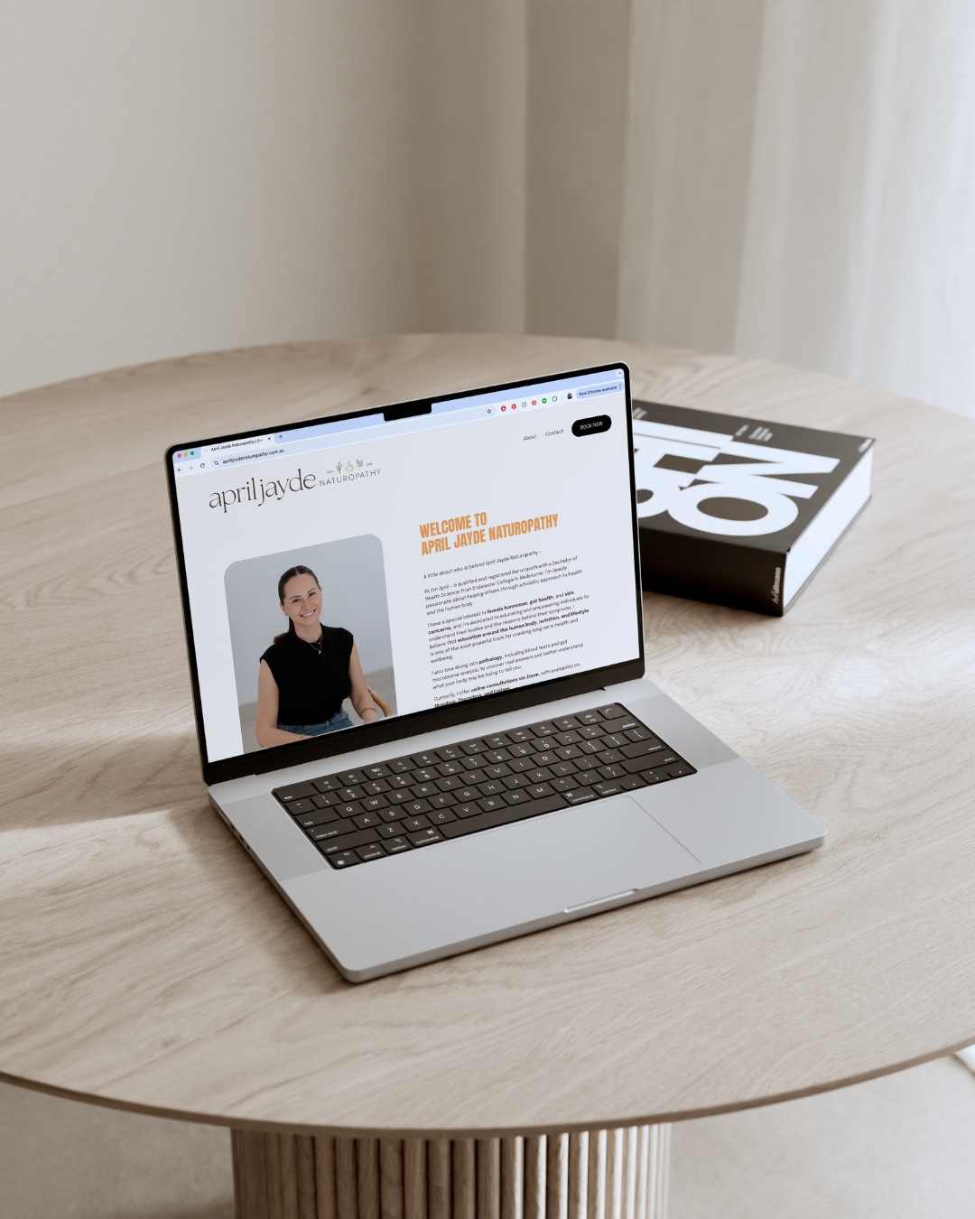 April Jayde Naturopathy website displayed on MacBook Pro laptop on round wooden pedestal table.