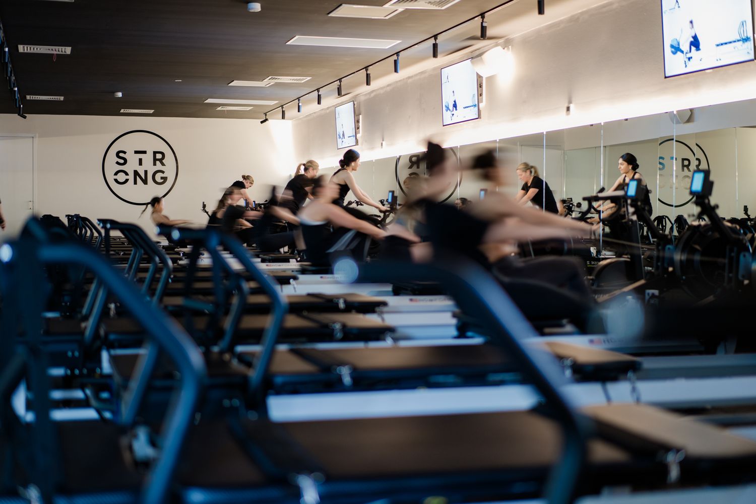 Group pilates reformer class in motion at STRONG studio with branded wall logo.