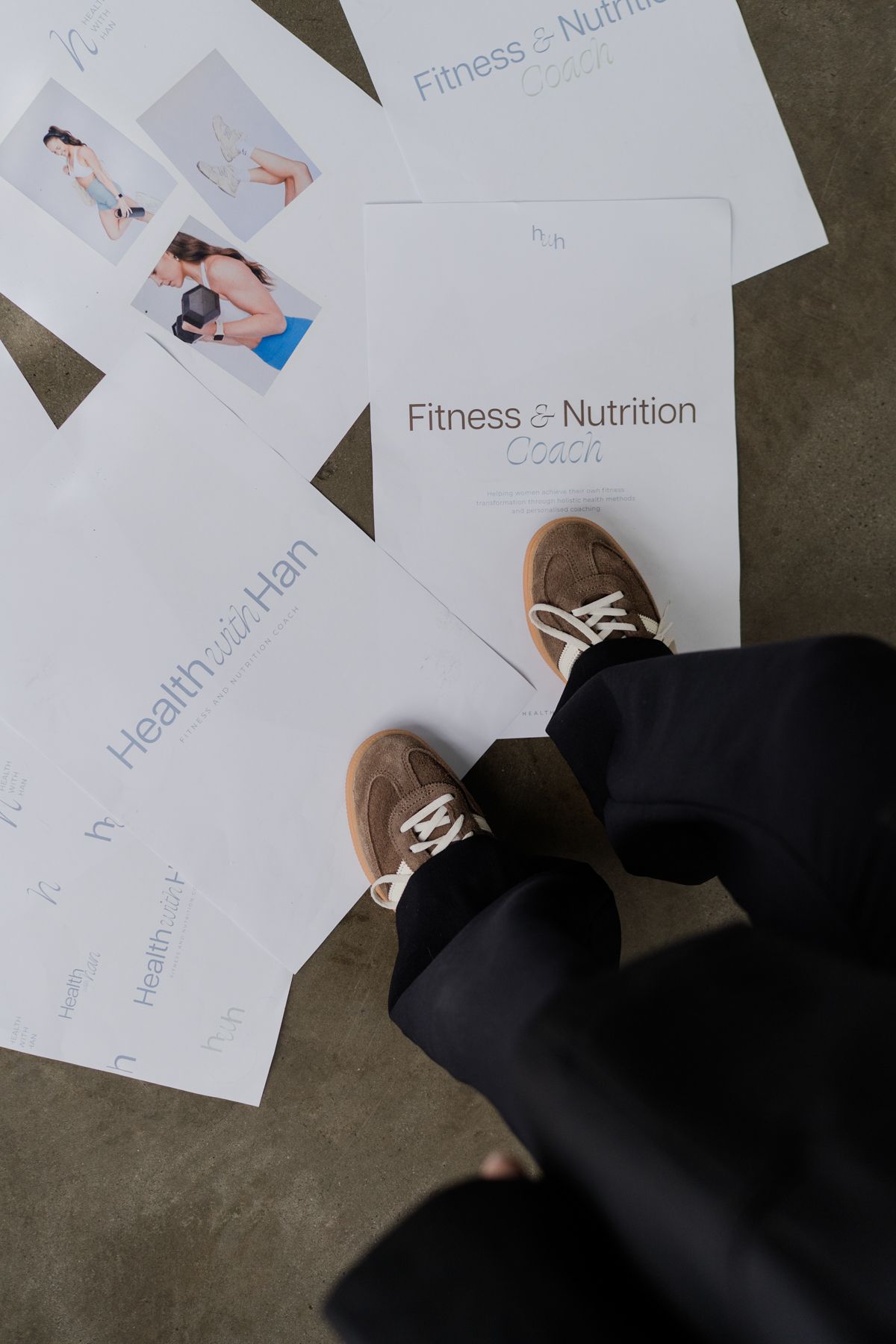 Overhead view of feet in tan sneakers standing among Health with Han fitness and nutrition coaching program papers.