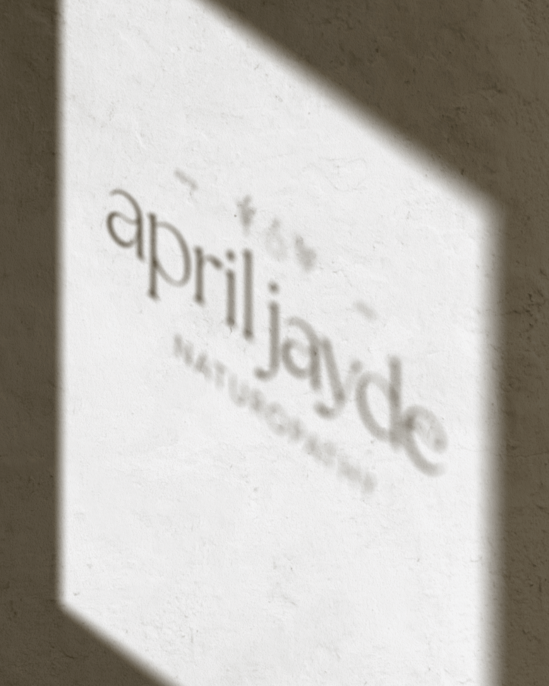 April Jayde Naturopathy logo elegantly displayed on a white wall with natural shadows.