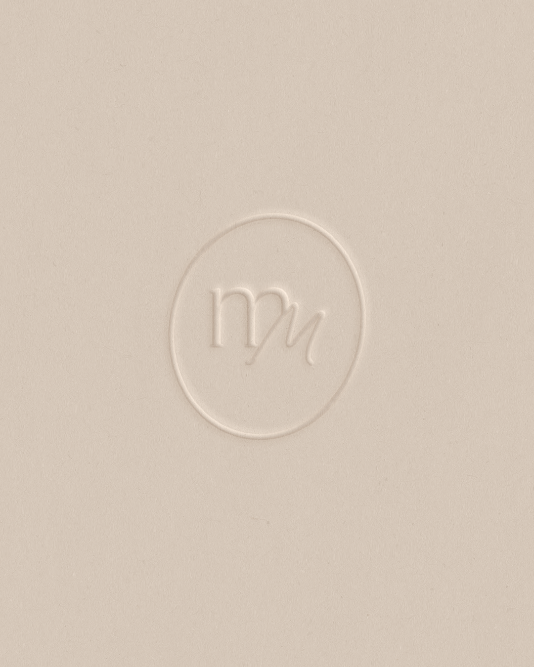 Elegant embossed mm monogram logo on a neutral beige textured background.