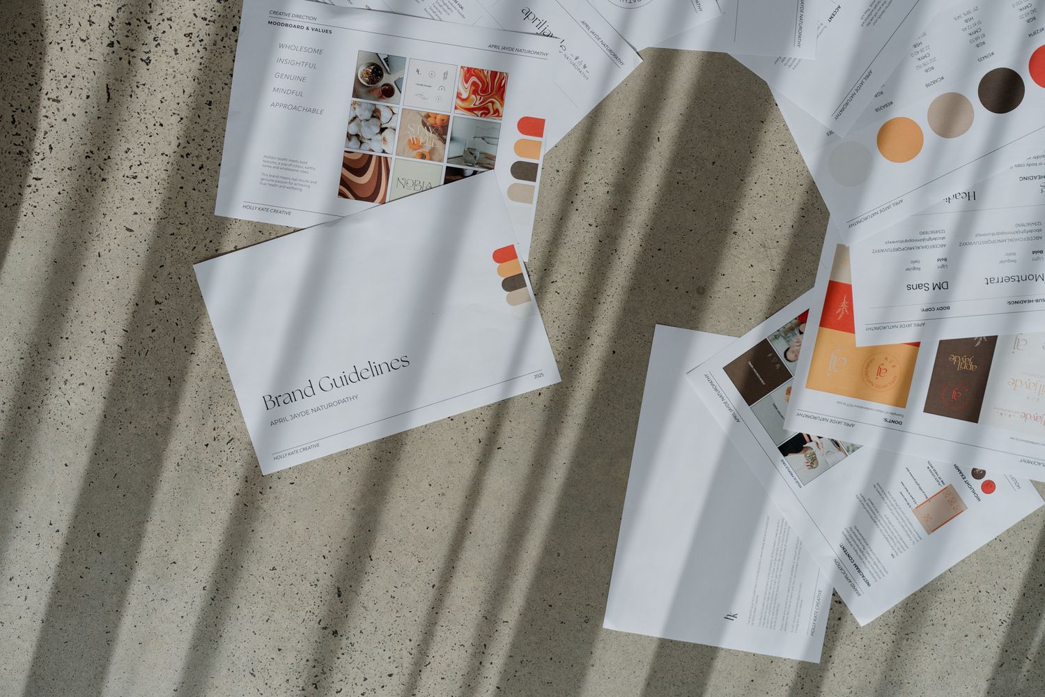 Brand guidelines documents with color swatches spread on a concrete surface in natural light.