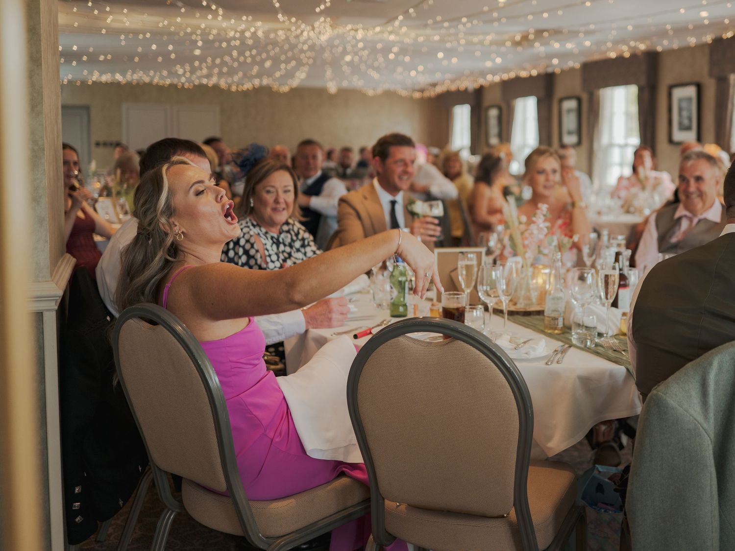 Wedding reception venue with string lights and upscale table settings where guests are seated at round tables.