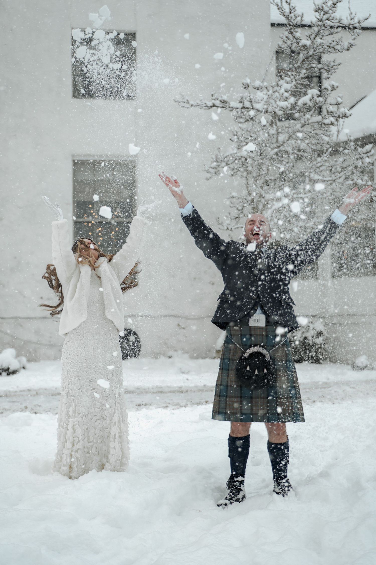 A couple plays in deep snow during their winter wedding celebration, throwing snow and laughing together.