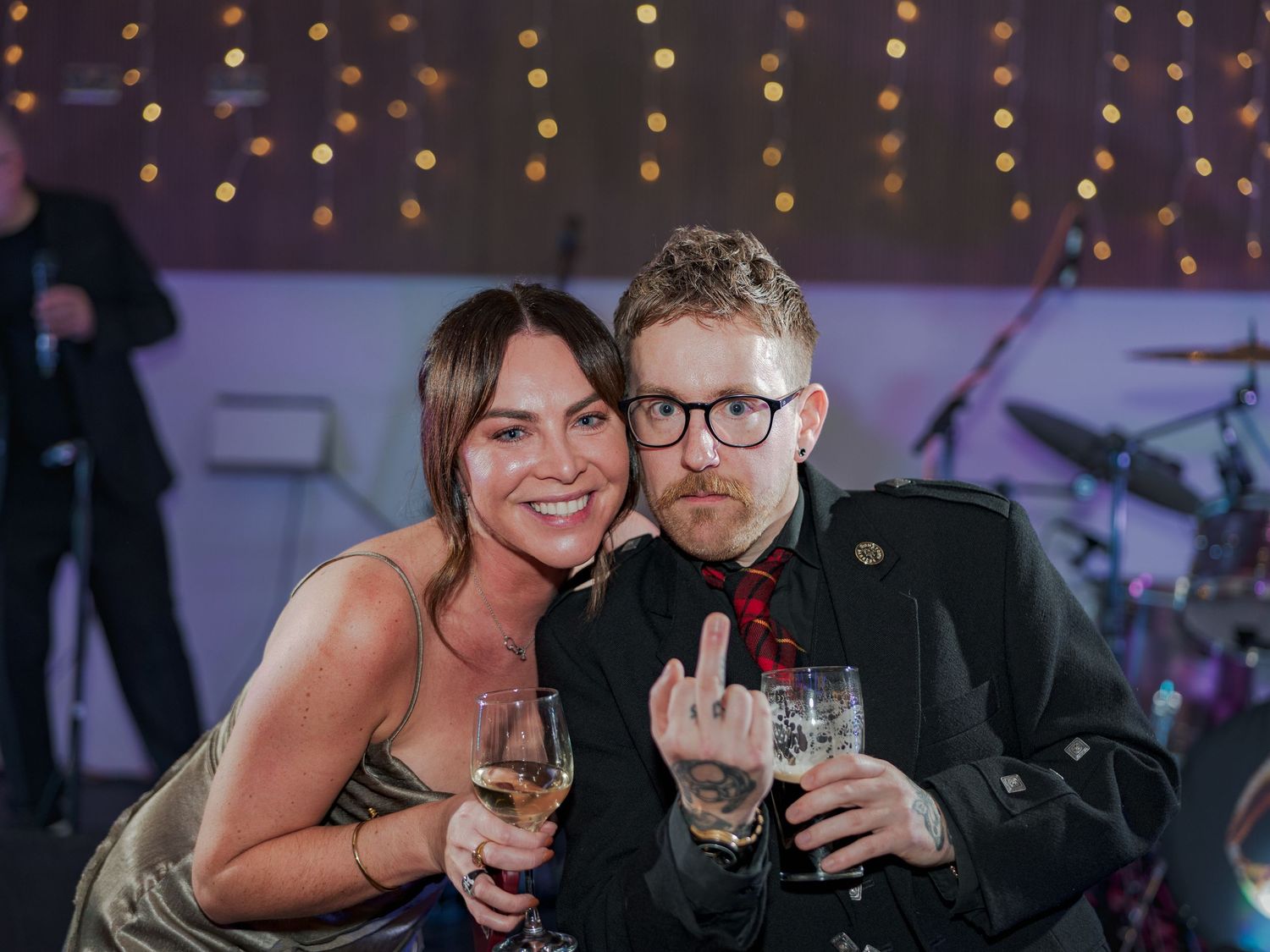 Party guests enjoying themselves with drinks and laughter under decorative string lights at an indoor celebration.