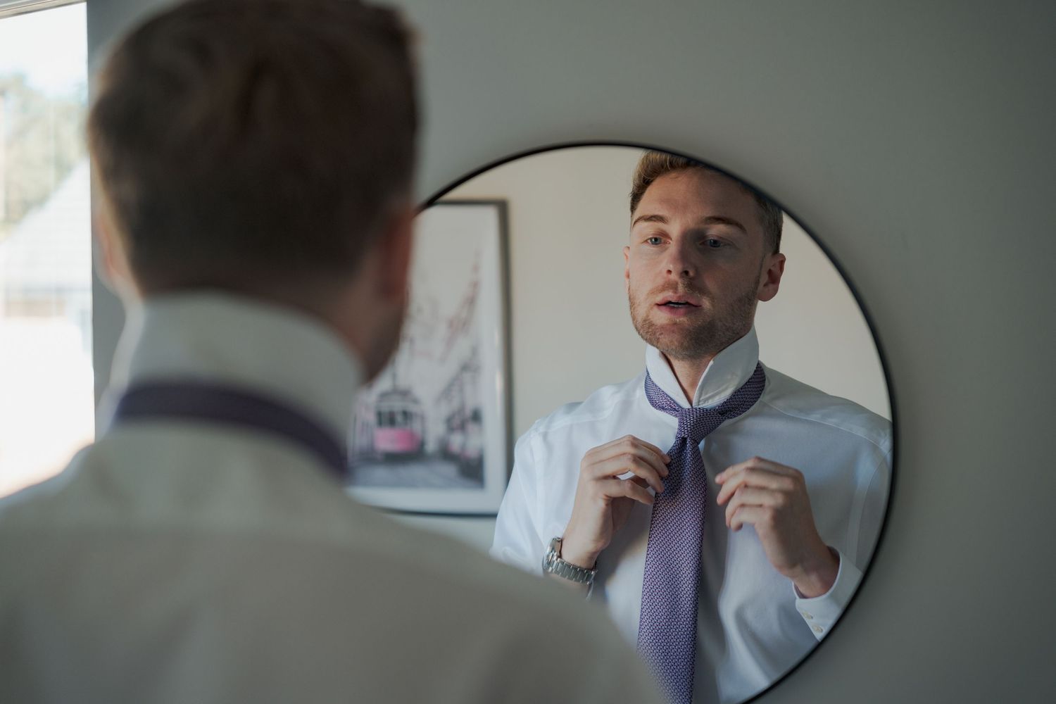 A person adjusts their tie while getting ready in front of a mirror.