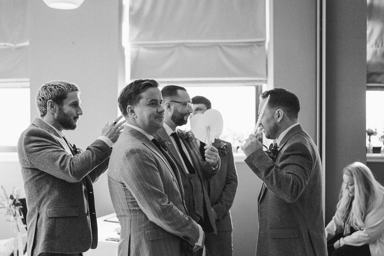 A group of men in suits and formal attire gather together in conversation at an indoor event in black and white.