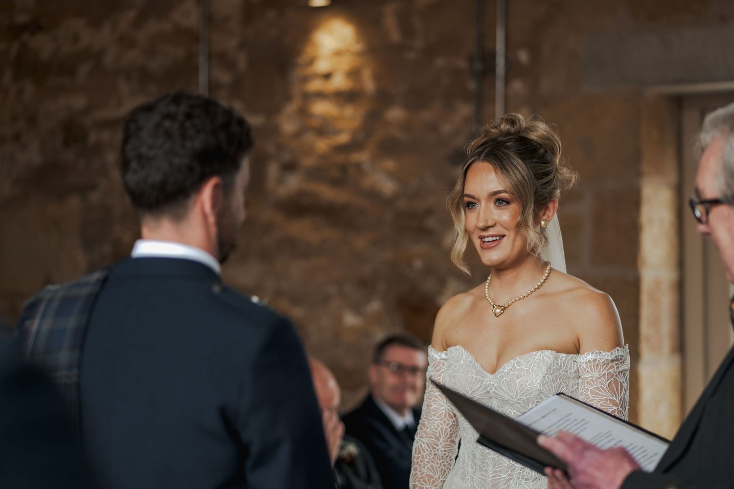 A couple shares a joyful moment during their wedding ceremony in a rustic stone-walled venue.