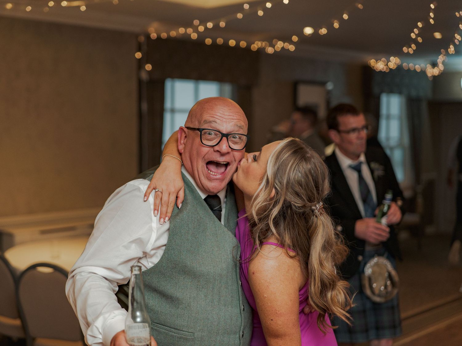 People sharing affectionate moments at a wedding reception under warm lighting and decorative string lights at Banchory Lodge.