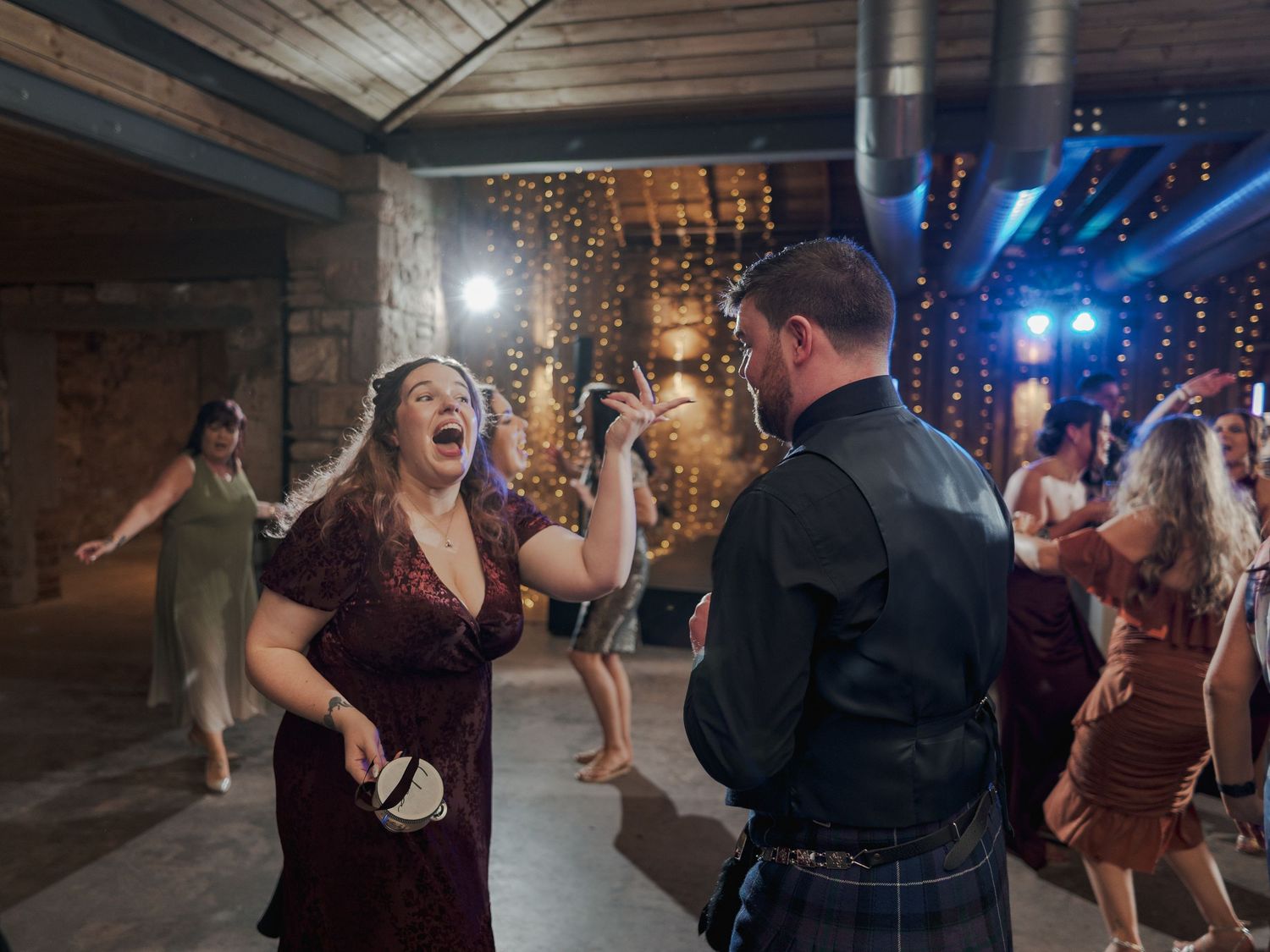 Guests dancing enthusiastically at a wedding reception in at Falside Mill with twinkle lights and blue lighting effects.
