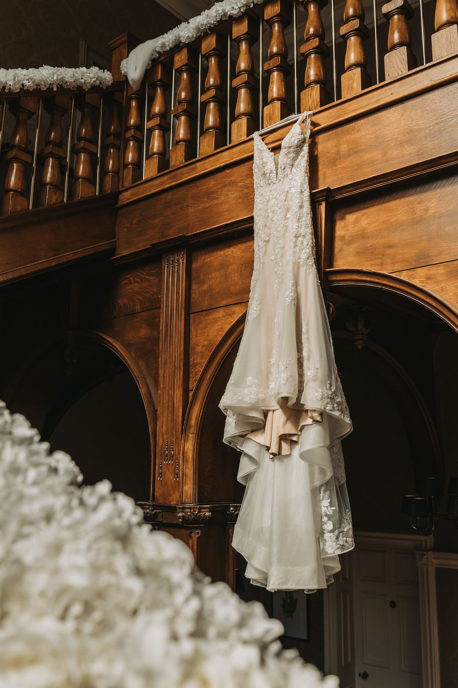 Elegant white lace wedding dress hangs on wooden paneled wall at Cornhill Castle with ornate architectural details.