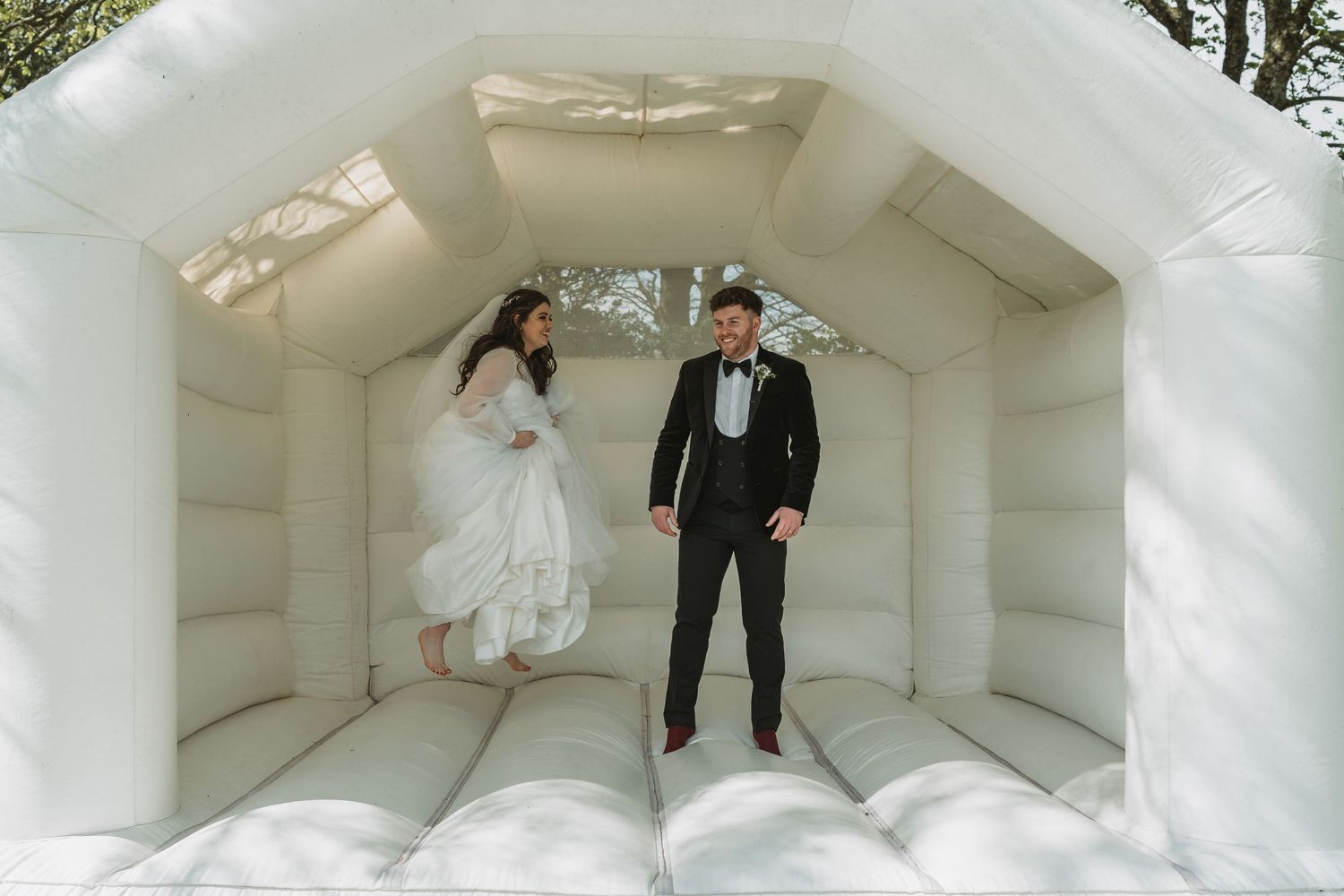 A bride and groom jump playfully inside an elegant all-white bouncy castle during their wedding celebration at Kinclune House.