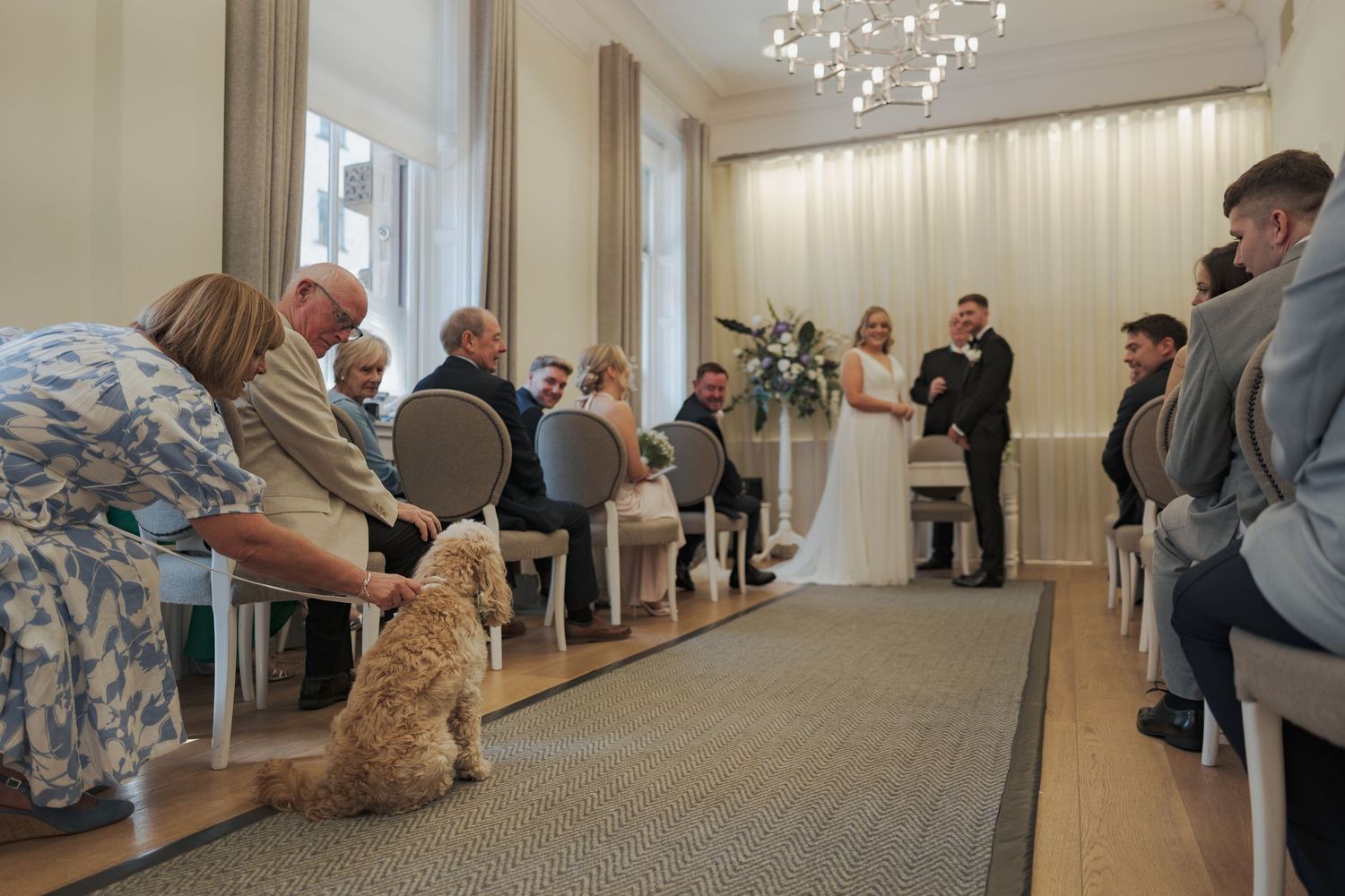 A group of people gather in an elegant room with chandeliers for what appears to be a dance or movement class.