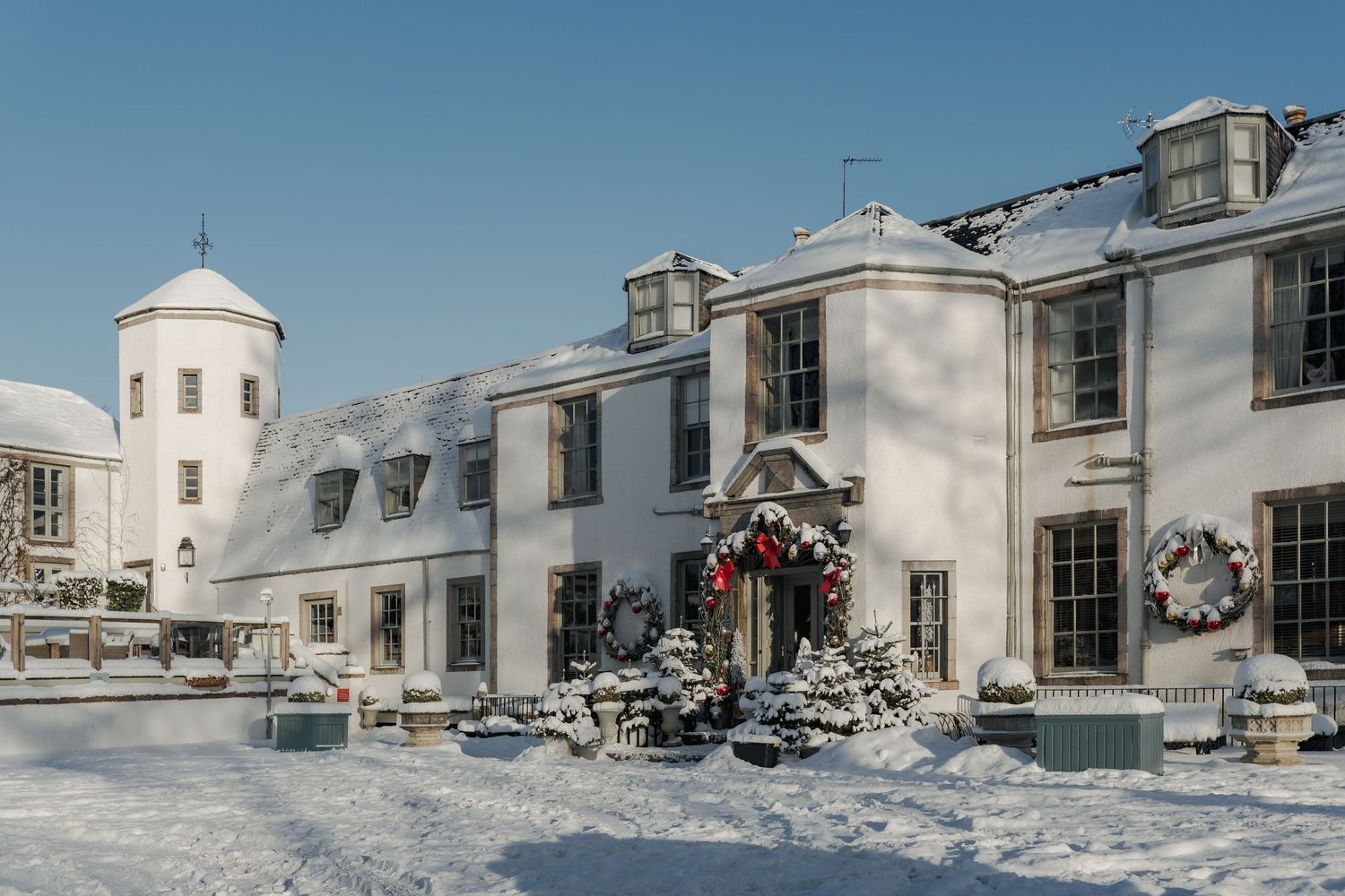 Snow-covered white manor house with Christmas wreaths and decorations on a bright winter day.