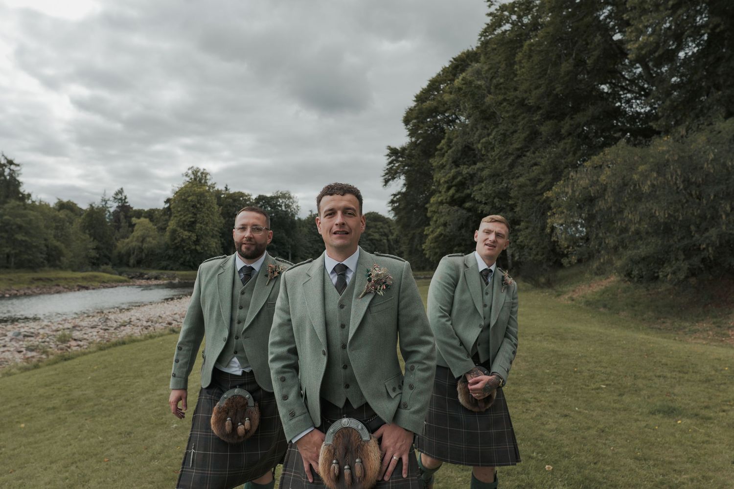 Six people in matching dark jackets stand and smile together in a grassy field on a cloudy day at Banchory Lodge.