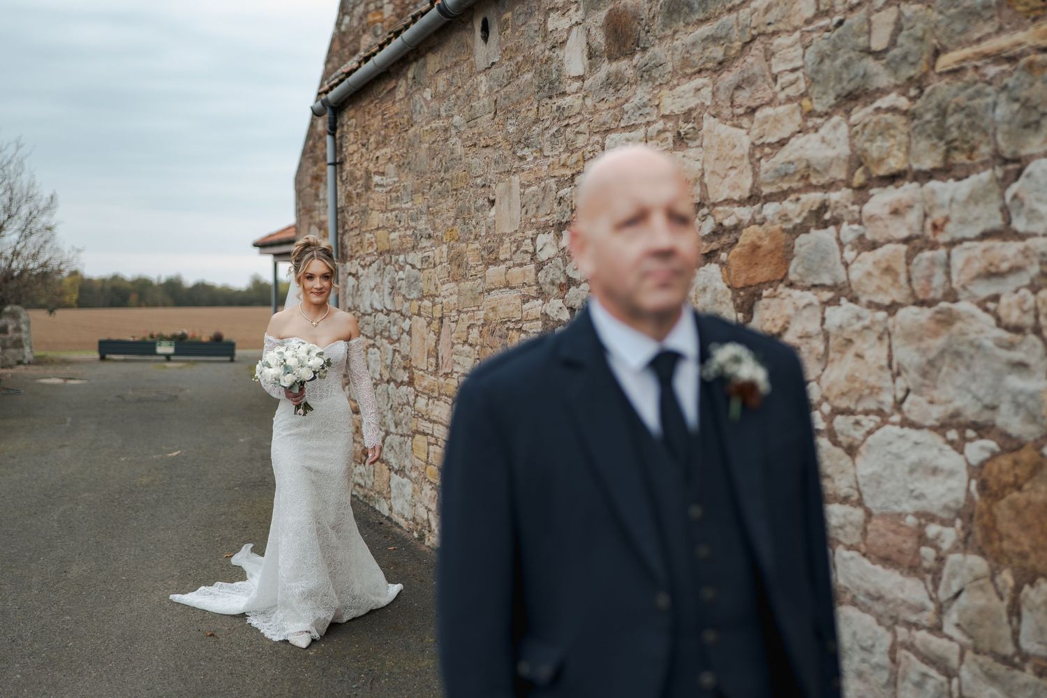 Wedding party gathered outside a rustic stone building for formal photographs.