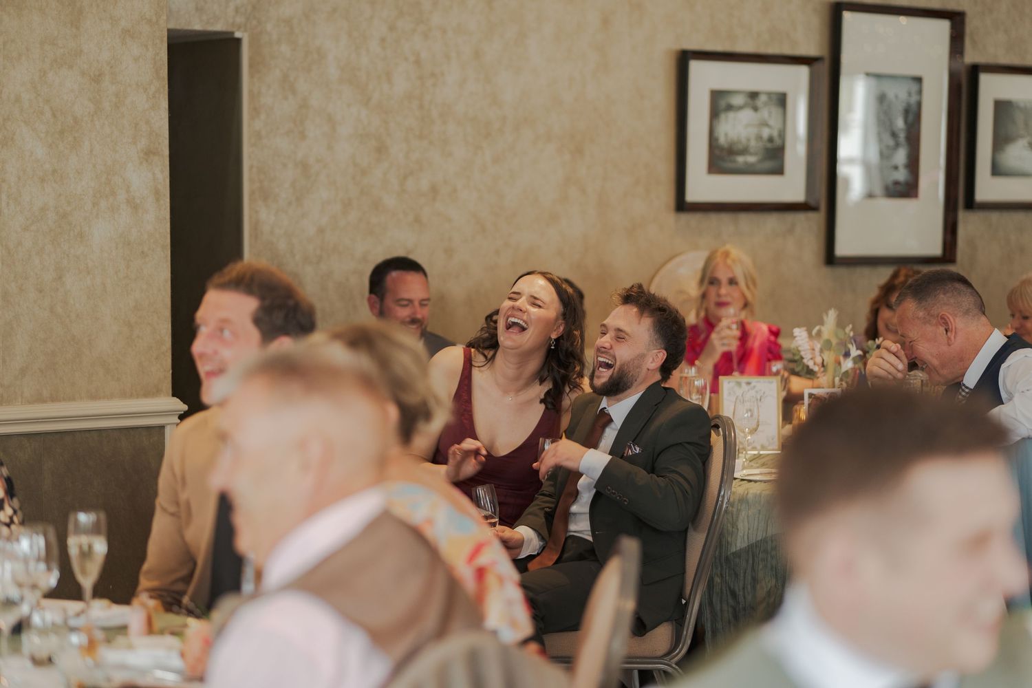Wedding guests laugh and smile while seated for dinner at a reception banquet table.