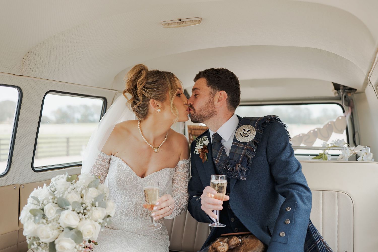 A romantic moment between newlyweds sharing champagne in a vintage white car decorated with wedding flowers.