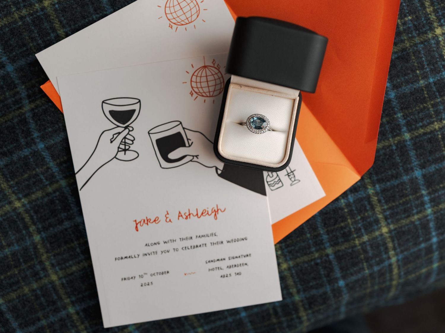 Wedding stationery and invitations displayed on a plaid fabric with handwritten details and elegant design elements.