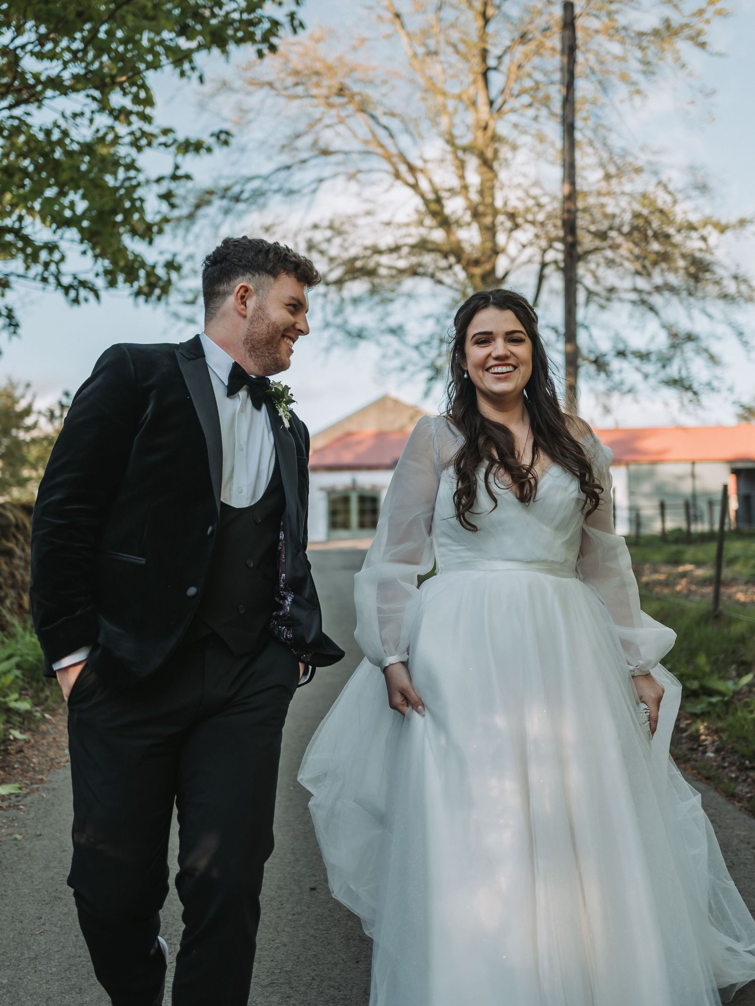 Elegant couple in black tuxedo and white flowing wedding dress share a joyful moment together outside in nature at Kinclune House.
