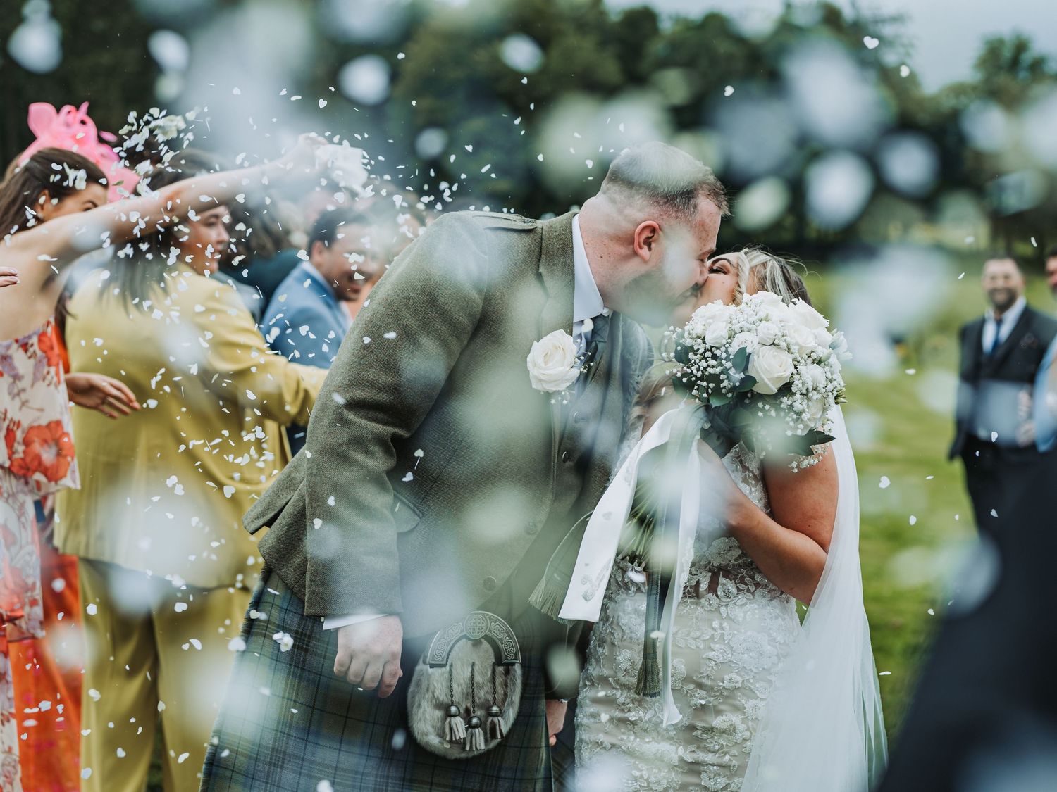 Wedding guests throw confetti during outdoor celebration at Cornhill Castle with Scottish kilts and formal attire.