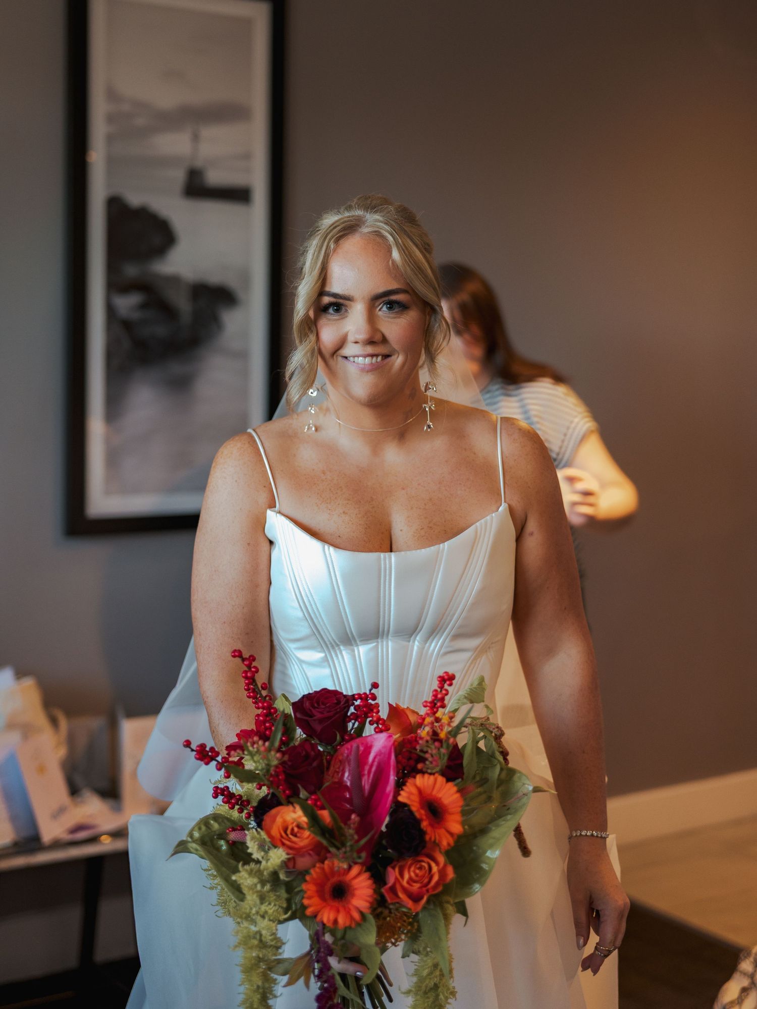 A bridal bouquet featuring vibrant orange, pink and red flowers with greenery against a warm interior background.